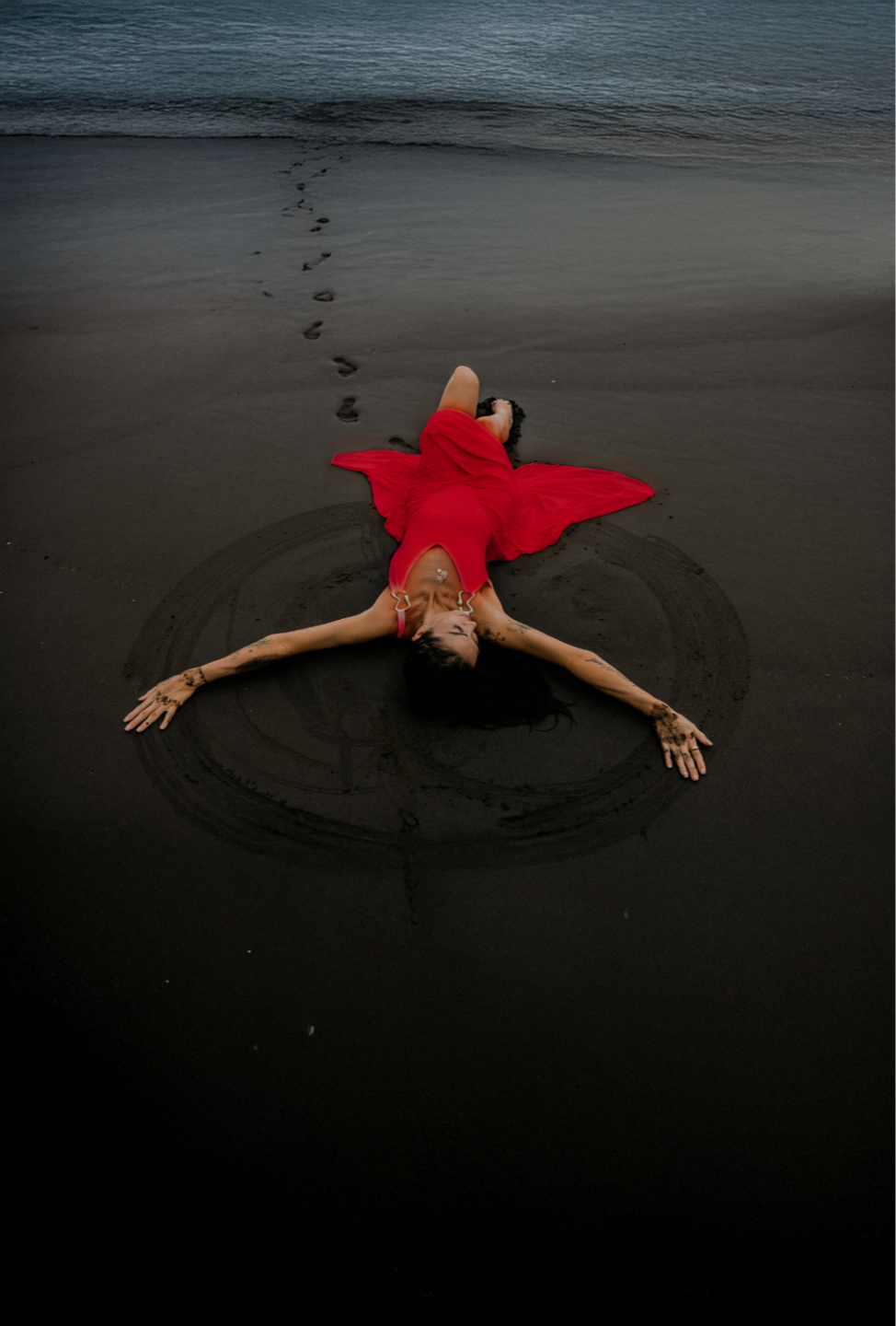 Woman in a red dress resting on a dark beach